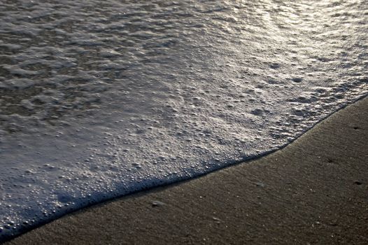 Waves coming ashore, at sunset, beach and foam.