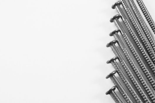 Close up of a group of steel nails arranged parallel and on the right portion of the image over white.