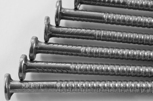Close up of several steel nails arranged parallel and over white.
