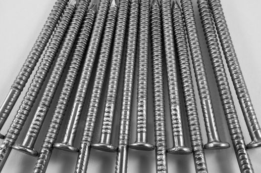 Close up of a group of steel nails arranged parallel and in a repetitive pattern over white.