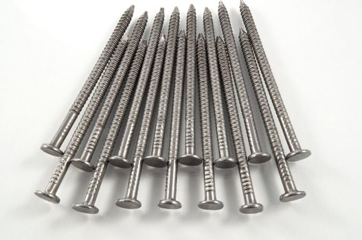 Close up of a group of steel nails arranged in a repetitive pattern over white.
