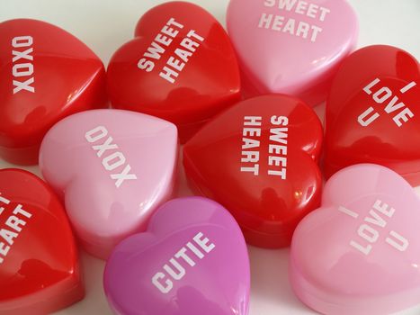 Plastic heart shaped boxes with various sayings in a love theme. Over white.