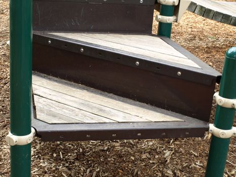 A set of stairs in a playground, bark dust on the ground underneath.