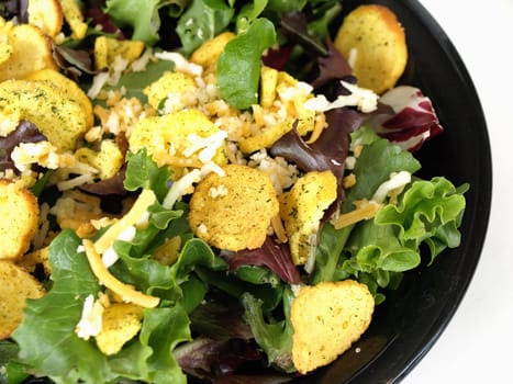 A tasty fresh greens salad with crutons and cheese in a black bowl.
