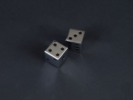 Two metal dice showing a score of seven on a black background.