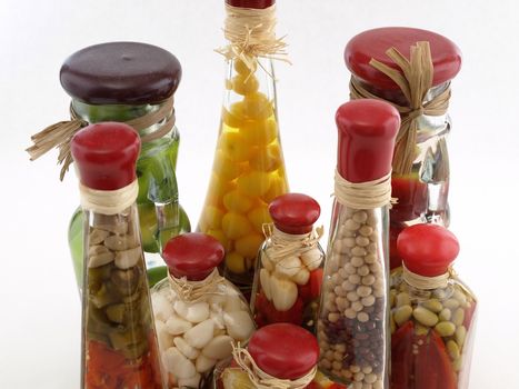 A colorful assortment of pickled spices in different shaped jars on white.