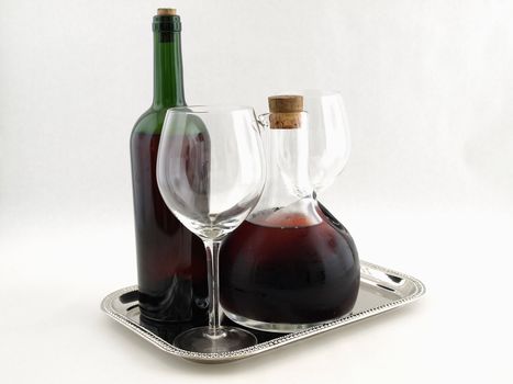Red wines and wine glasses on a silver platter over a white background.