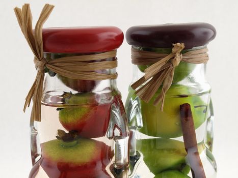Glass jars filled with green apples and red pomegranates, on a white background.