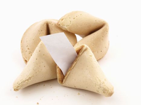 A broken fortune cookie with whole cookies over a white background. Cookie has blank fortune sticking out of one side.
