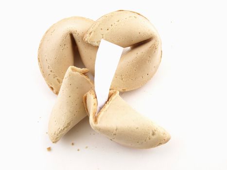 A broken fortune cookie with whole cookies over a white background. Cookie has blank fortune sticking out of one side.