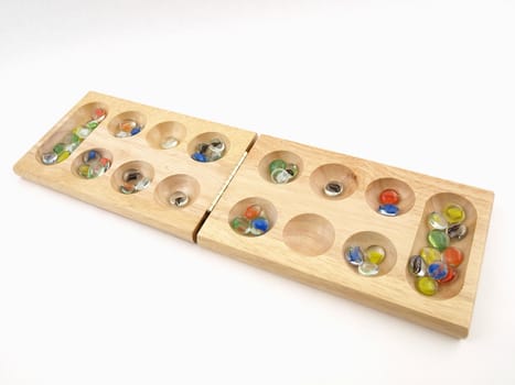 A folding wooden Mancala board game with glass stone pieces, isolated against a white background.