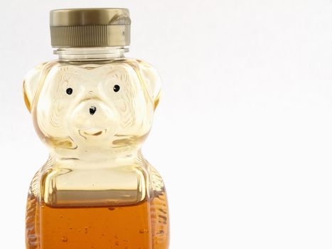 A plastic bear shaped container half full of honey over a white background. Offset with room for text.