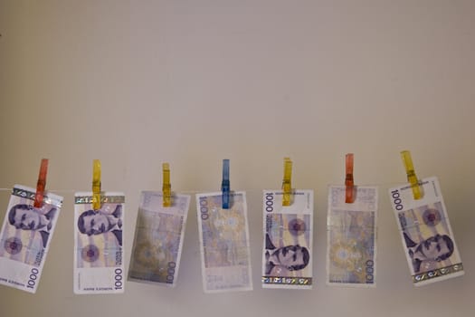 Illustration with the highest denomination of bank notes in Norway, hanging on a clothes hanger with clothes-pegs. Could illustrate money laundering and illegal business, but also a good illustration for wealth and money.  Space for printing / design over the money.