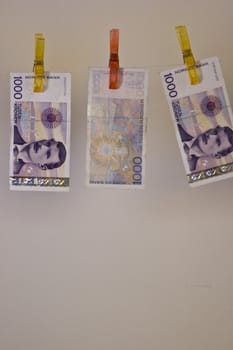 Illustration with the highest denomination of bank notes in Norway, hanging on a clothes hanger with clothes-pegs. Could illustrate money laundering and illegal business, but also a good illustration for wealth and money.  Space for printing / design beneath the money.