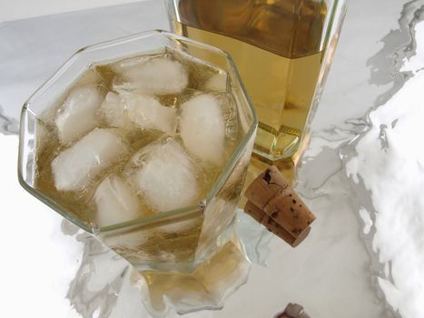 A glass on alcohol with ice, a bottle and a cork isolated on a reflective back ground