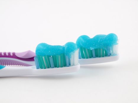 Two toothbrushes with a blue gel toothpaste over a white background.