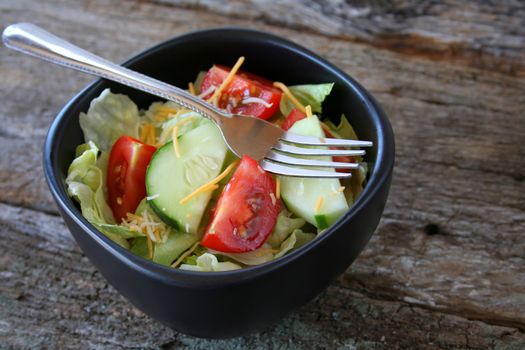 Fresh house salad in a black bowl with a fork.  All done on an old wood textured background.  Copy space also available.