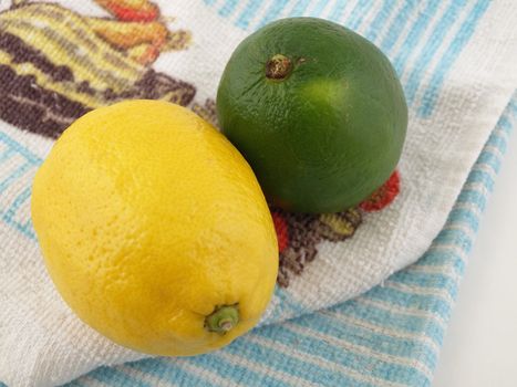 A yellow lemon and a green lime on a blue kitchen towel.