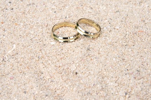 A pair of gold wedding rings delicately placed in the sand on a tropical beach