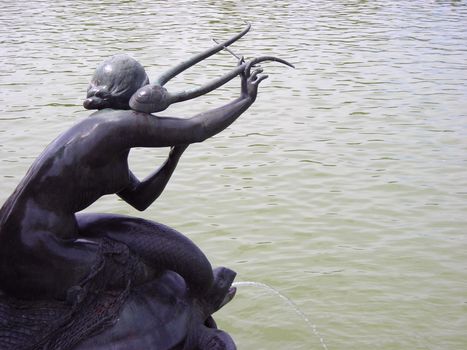 Sculpture of a siren playing lyre on top of a turtle with the Retiro Gardens Lake in front of her.