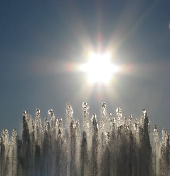 Water fountain spray with a sun starburst overhead.
