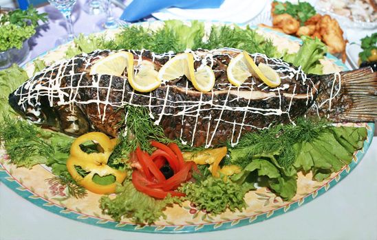 Roasted sea fish with leimon, tomatos, lettuce on table.