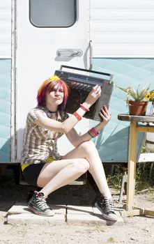 Punk girl with brightly colored hair sitting on trailer step holding boom box