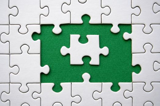 White jigsaw puzzle frame on green background with one jigsaw puzzle piece in the middle