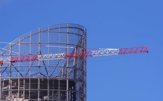 Part of a crane with modern building under construction on a blue sky background