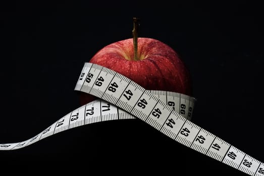 A delicious red apple with at measuring tape around it