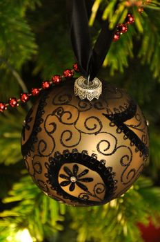 Richly decorated Christmas ball (black on gold) hanging in tree with lights and decoration