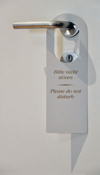 Typical hotel tag "Please do not disturb" (text in English and German) hanging at modern hotel door handle with great shadows - large space for your own text!