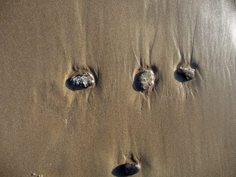 Some stones standing on some beach sand.