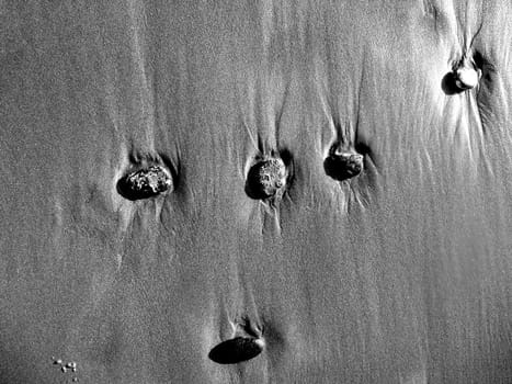 Some stones standing on some beach sand.