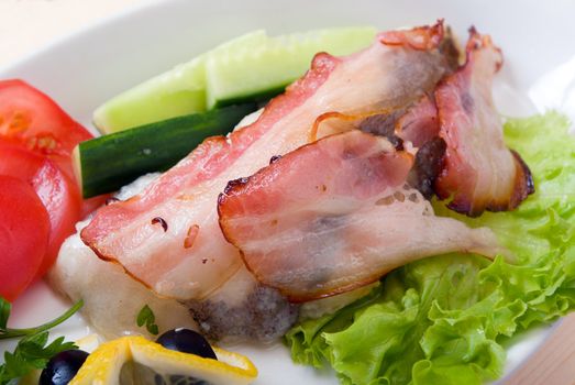 The halibut prepared with vegetables and bacon.close up