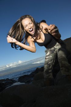 Mid-adult Caucasian woman at rocky beach leaning into camera holding out fists and yelling.