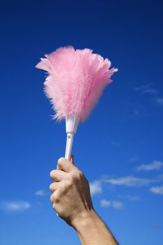 Close up of young female adult Caucasian's hand holding feather duster against sky.