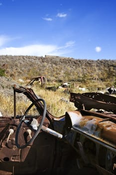 Driver's wheel of old abandoned and rusted car in field.