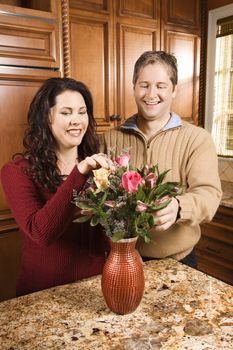 Caucasian woman and man smiling and arranging flowers together in kitchen.
