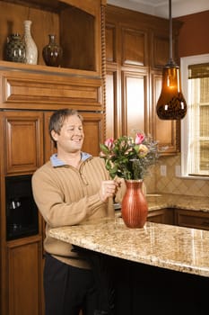 Caucasian man smiling and arranging flowers in vase in kitchen.