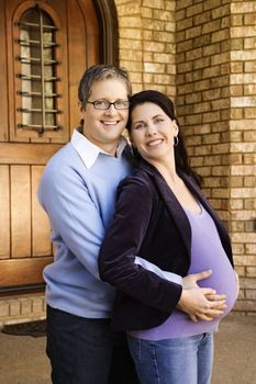 Portrait of adult male and pregnant female embracing near doorway.