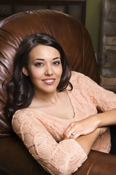 Caucasian/Hispanic young woman sitting in leather chair smiling with arms crossed looking at viewer.