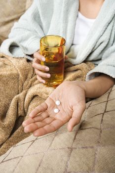 Caucasian/Hispanic young woman holding pills in hand with glass of water.