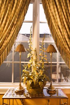 Interior view of window with curtains pulled back and decorative table with lamps and plant.