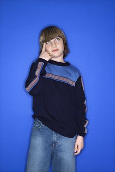 Portrait of Caucasian boy with one hand pointing at his head standing against blue background.