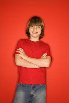 Portrait of Caucasian boy in studio standing against red background with arms crossed.