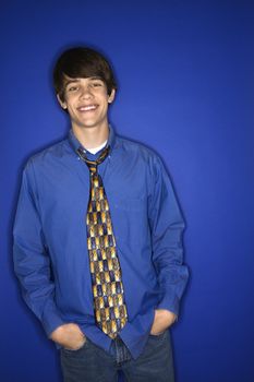 Portrait of Caucasian teen boy standing with hands in pockets against blue background.