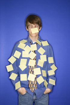 Portrait of Caucasian teen boy standing against blue background covered with blank sticky notes.