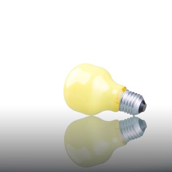 Yellow lightbulb with reflection on glass surface.