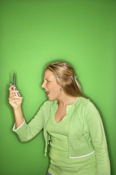 Portrait of blond Caucasian teen girl looking at cellphone with shock and disbelief against green background.